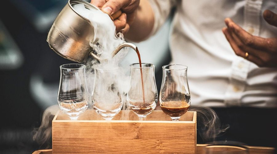 Barista pouring brewed coffee during a controlled tasting session, representing competition-level coffee lots that influenced how quality is evaluated in specialty coffee