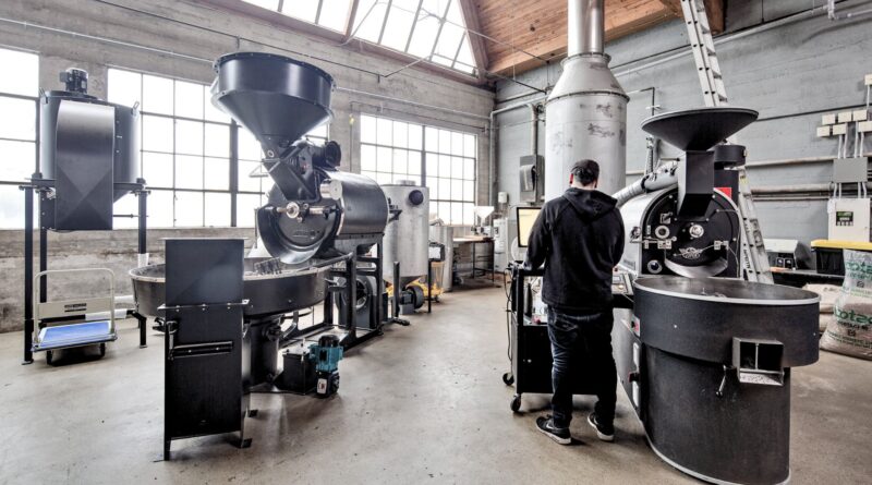 Coffee roastery production floor showing multiple drum roasters and an operator managing batch roasting capacity