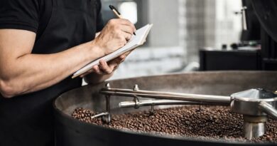 Coffee roaster monitoring beans in a roasting drum, illustrating how green coffee sourcing decisions affect production consistency and roast performance.”