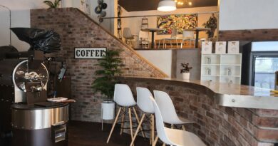 A combined coffee roastery and café interior showing a commercial roaster beside a customer-facing bar and seating area, illustrating the operational challenges of shared production and hospitality spaces.