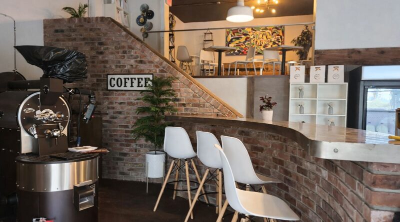 A combined coffee roastery and café interior showing a commercial roaster beside a customer-facing bar and seating area, illustrating the operational challenges of shared production and hospitality spaces.