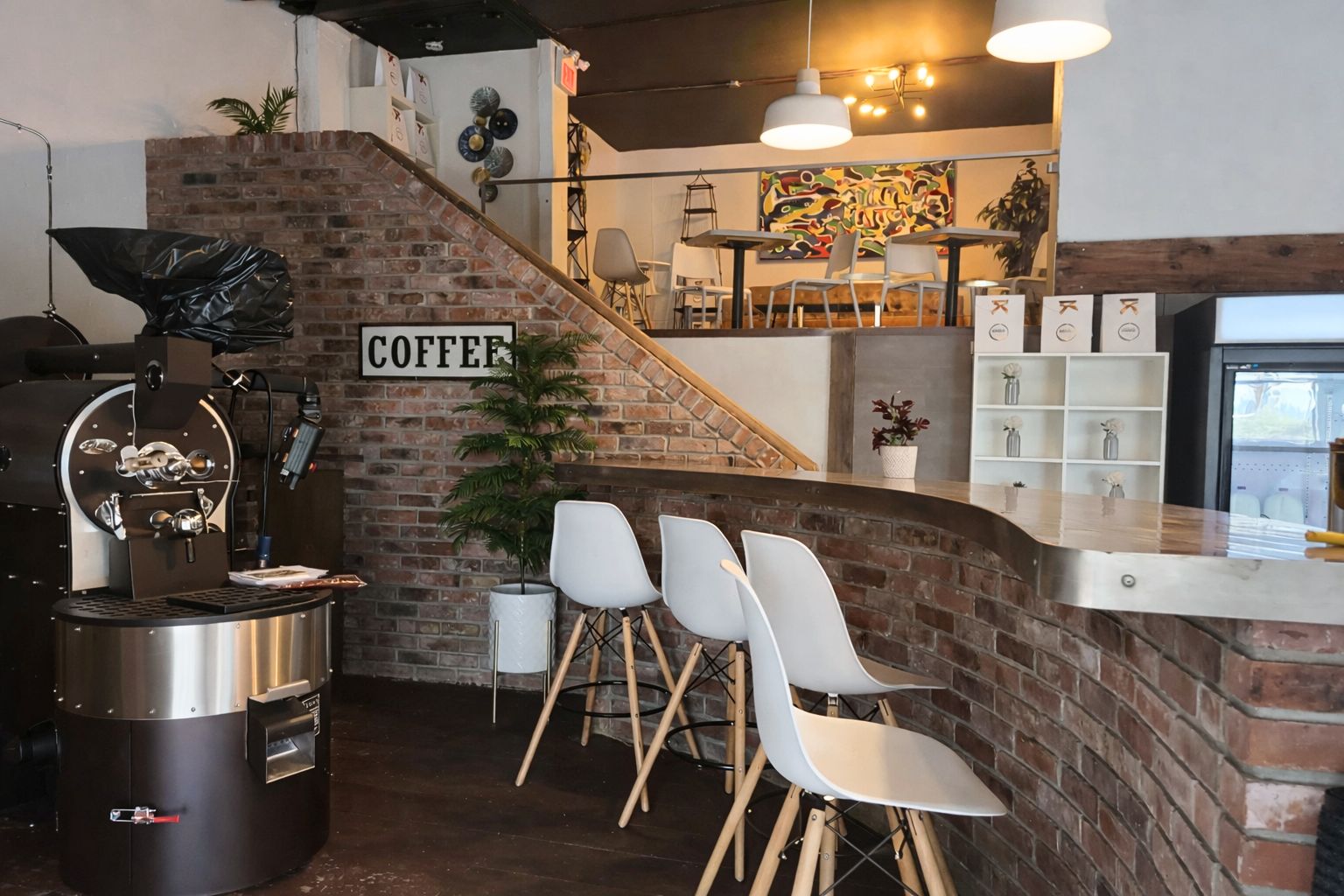 A combined coffee roastery and café interior showing a commercial roaster beside a customer-facing bar and seating area, illustrating the operational challenges of shared production and hospitality spaces.