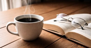 “A steaming cup of coffee on a wooden table beside an open book, representing how coffee enhances focus, comfort, and daily enjoyment”
