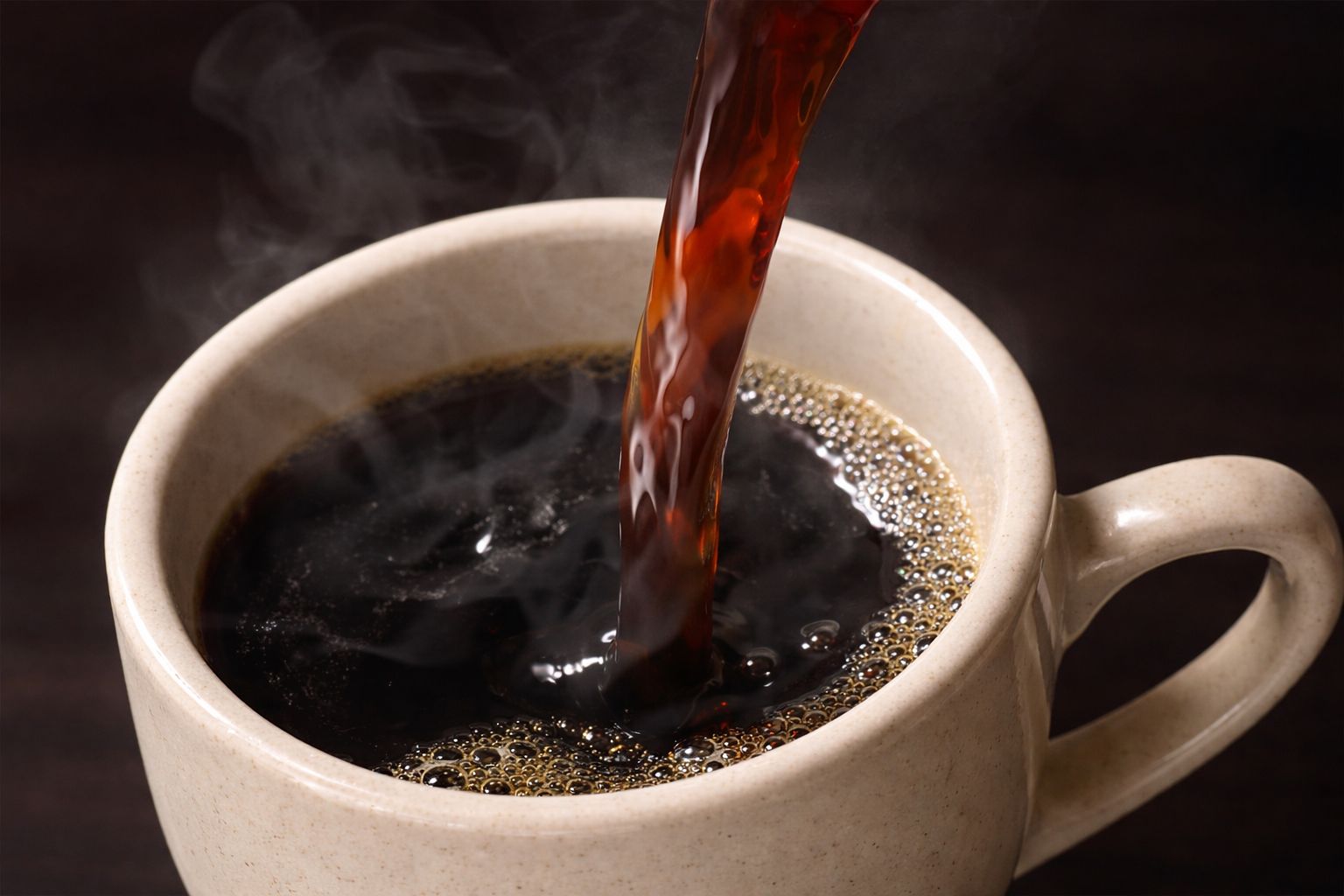 Hot black coffee being poured into a ceramic cup.